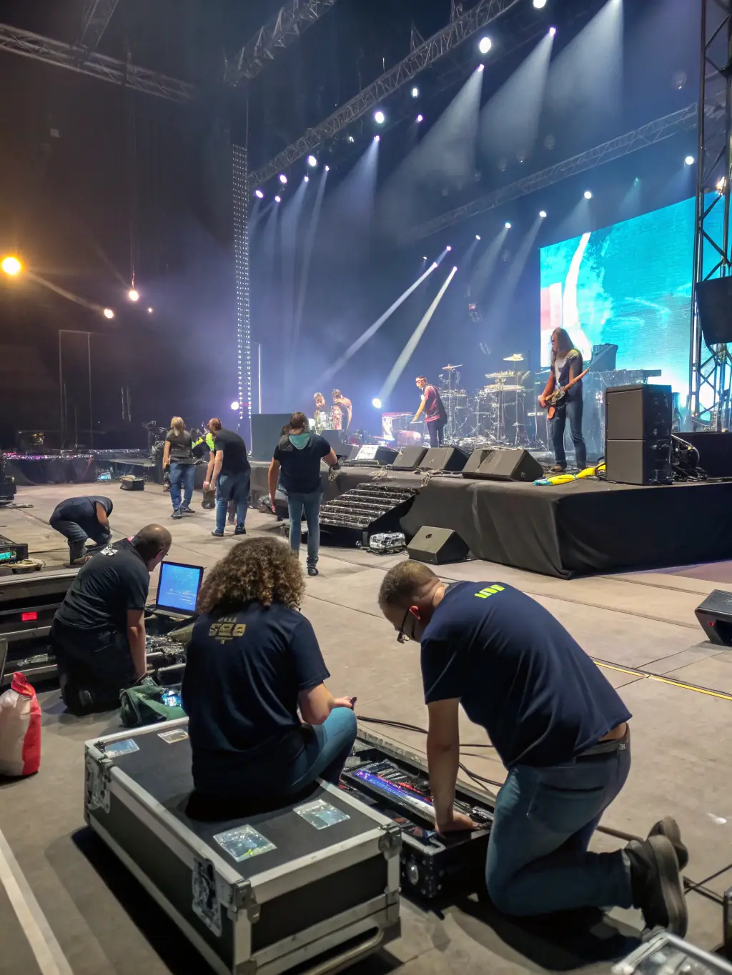 A diverse group of volunteers setting up sound equipment at a community event, with banners promoting Association Timeless and electronic music in the background.